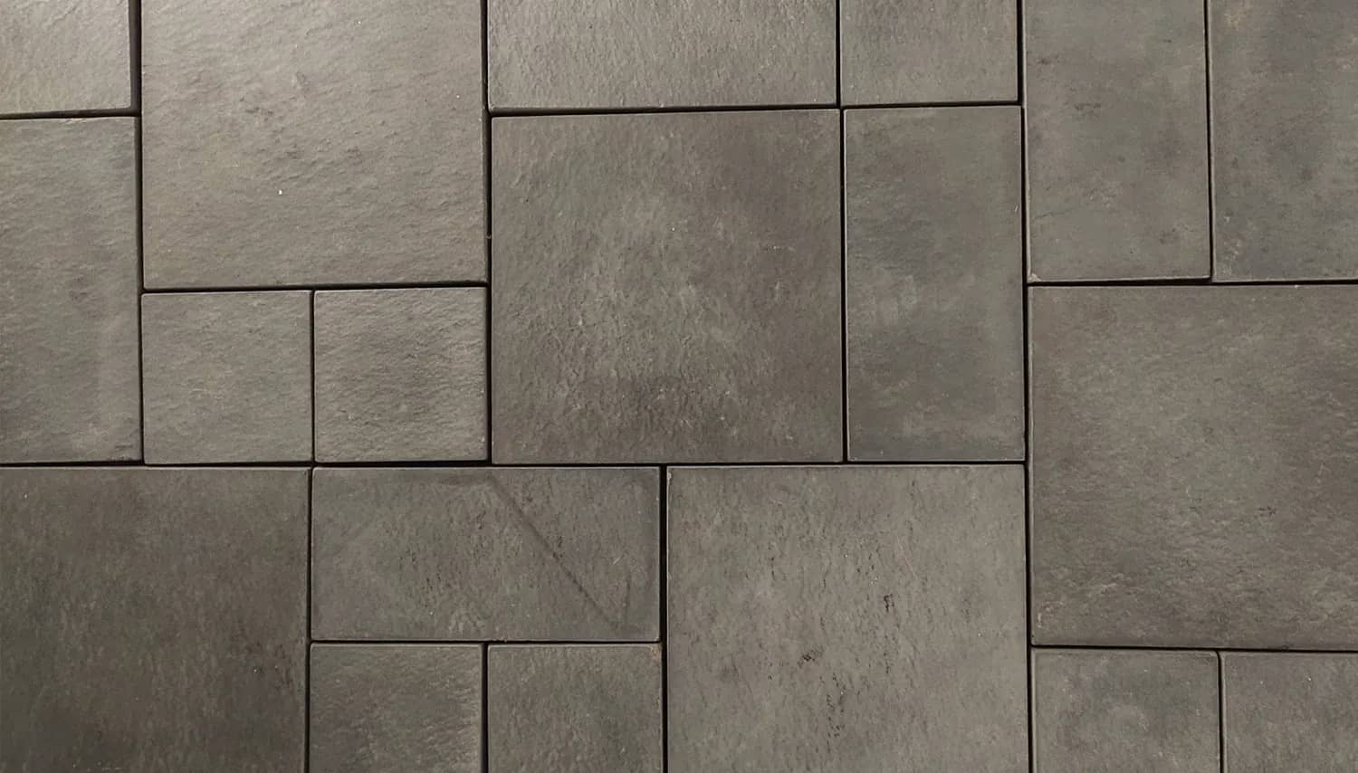 Charcoal concrete driveway paving in mixed formats, coursed into a repeating modular panel with tight joints