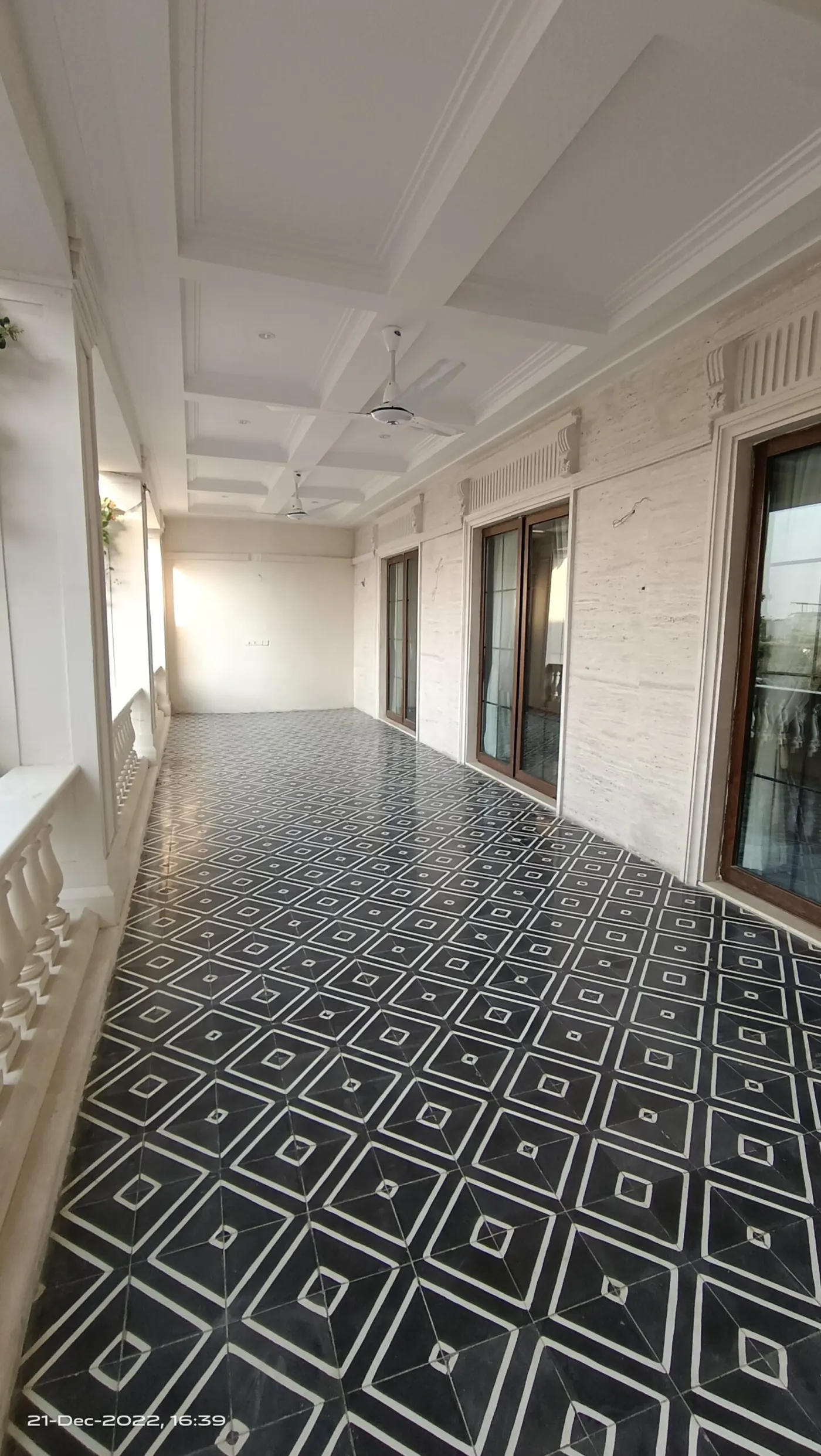 Charcoal and white diamond pattern cement tile floor running the length of a verandah with travertine clad walls