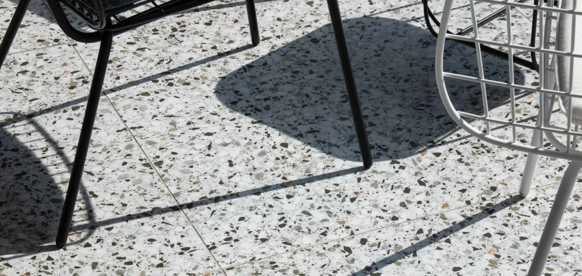 Polished terrazzo floor in raking afternoon light, chair legs casting long shadows across the aggregate