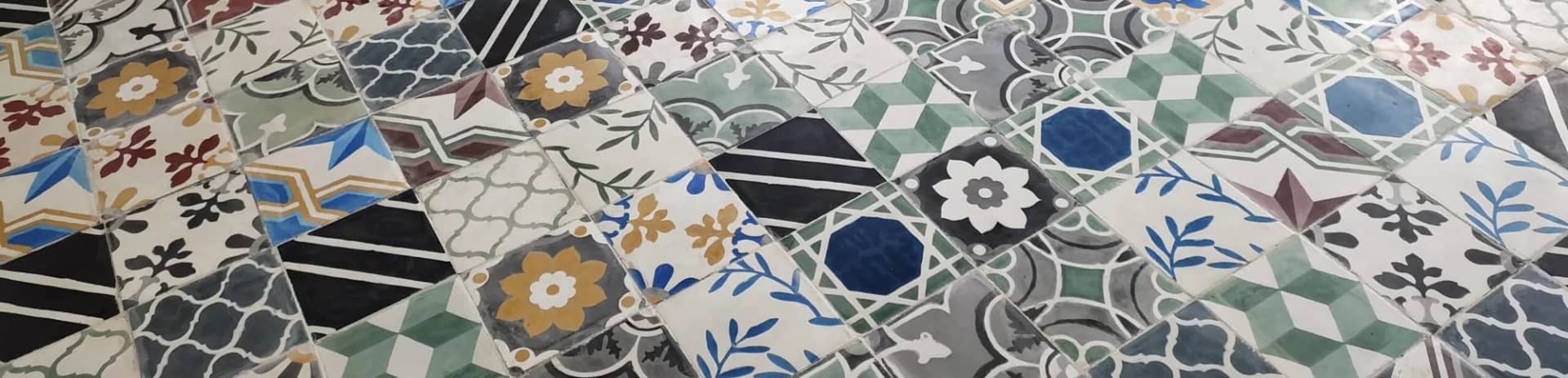 Moroccan pattern cement tiles laid on the diagonal as a patchwork of florals, stars and geometrics in green, ochre, blue and black