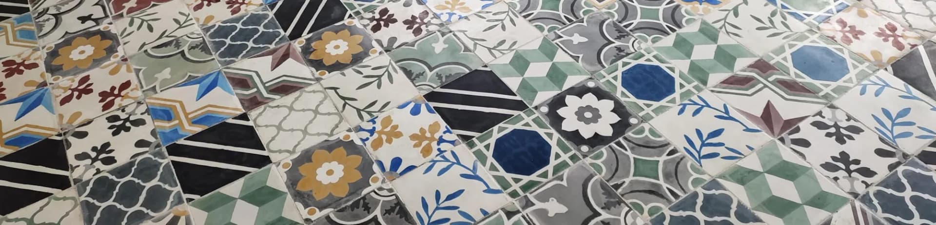 Moroccan pattern cement tiles laid on the diagonal as a patchwork of florals, stars and geometrics in green, ochre, blue and black