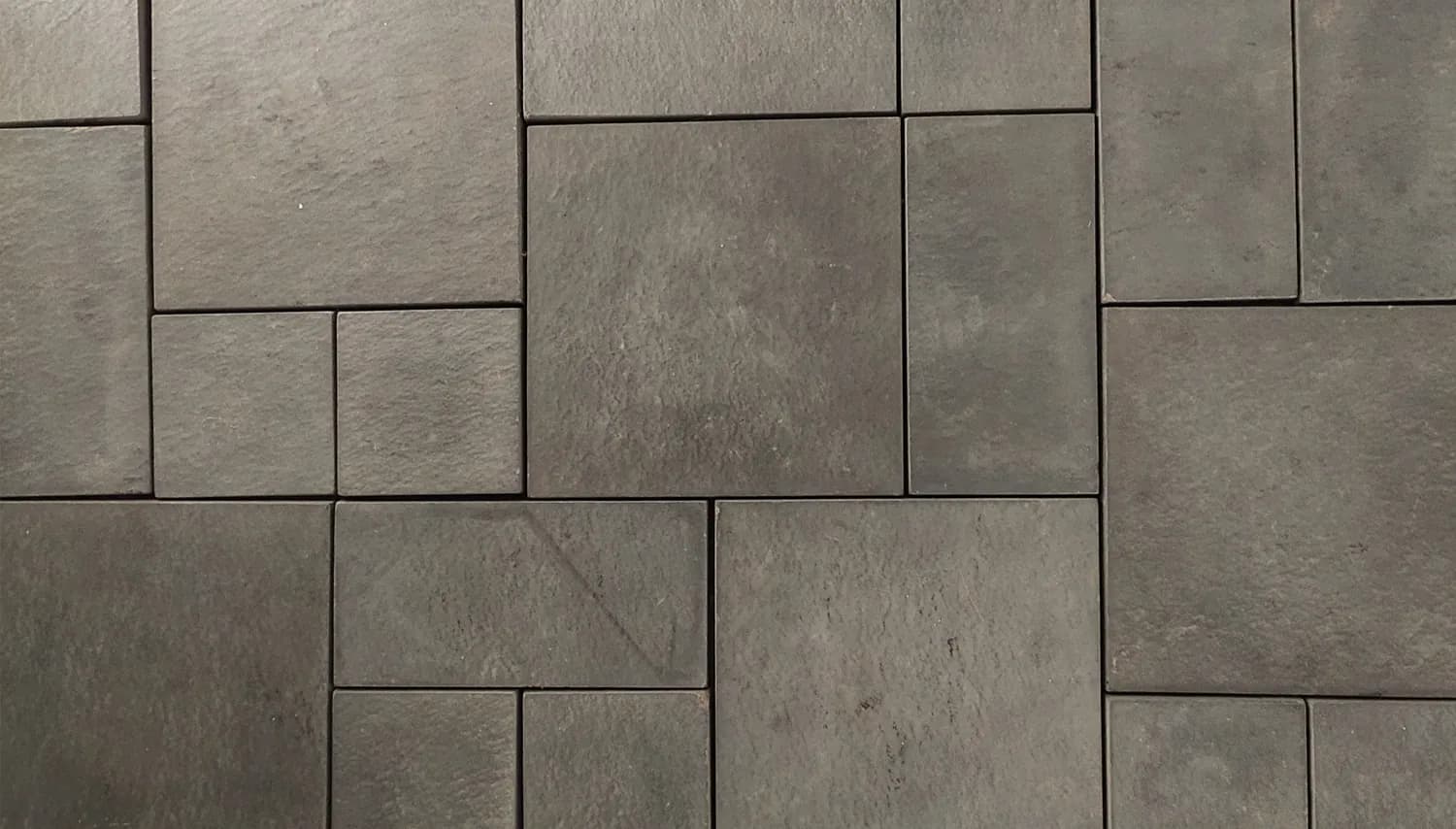 Charcoal concrete driveway paving in mixed formats, coursed into a repeating modular panel with tight joints