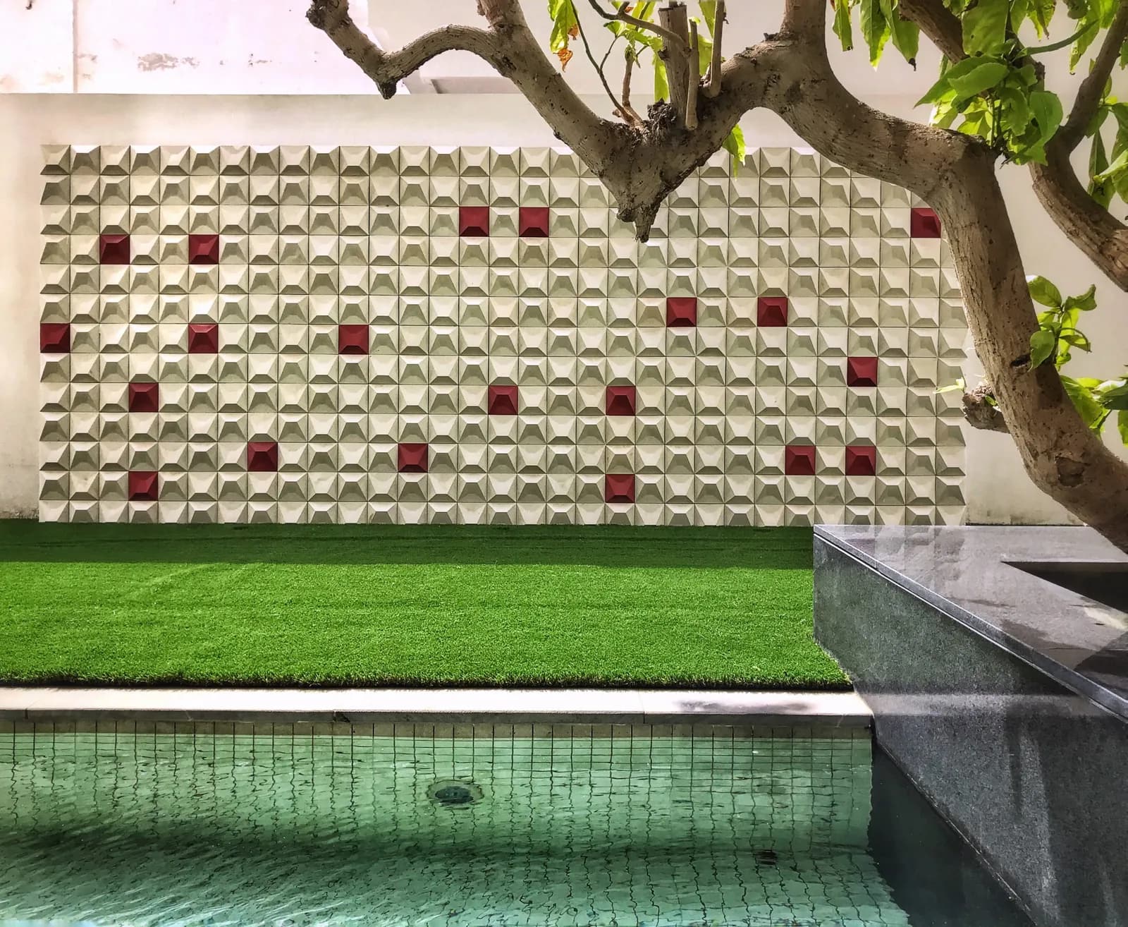 Kirthar 3D concrete tiles in cream with single deep red units scattered through the field, on a poolside garden wall