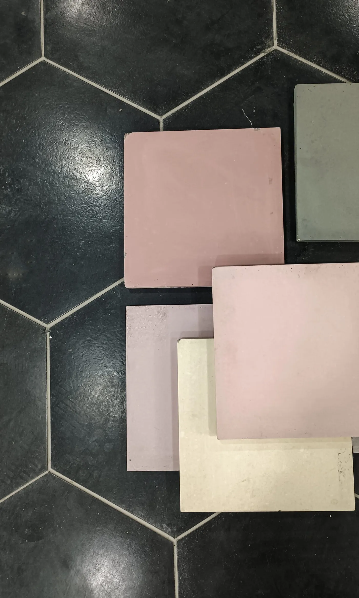 Plain pigmented cement tiles in pink, mauve, sage and cream laid out on a dark hexagonal tiled floor